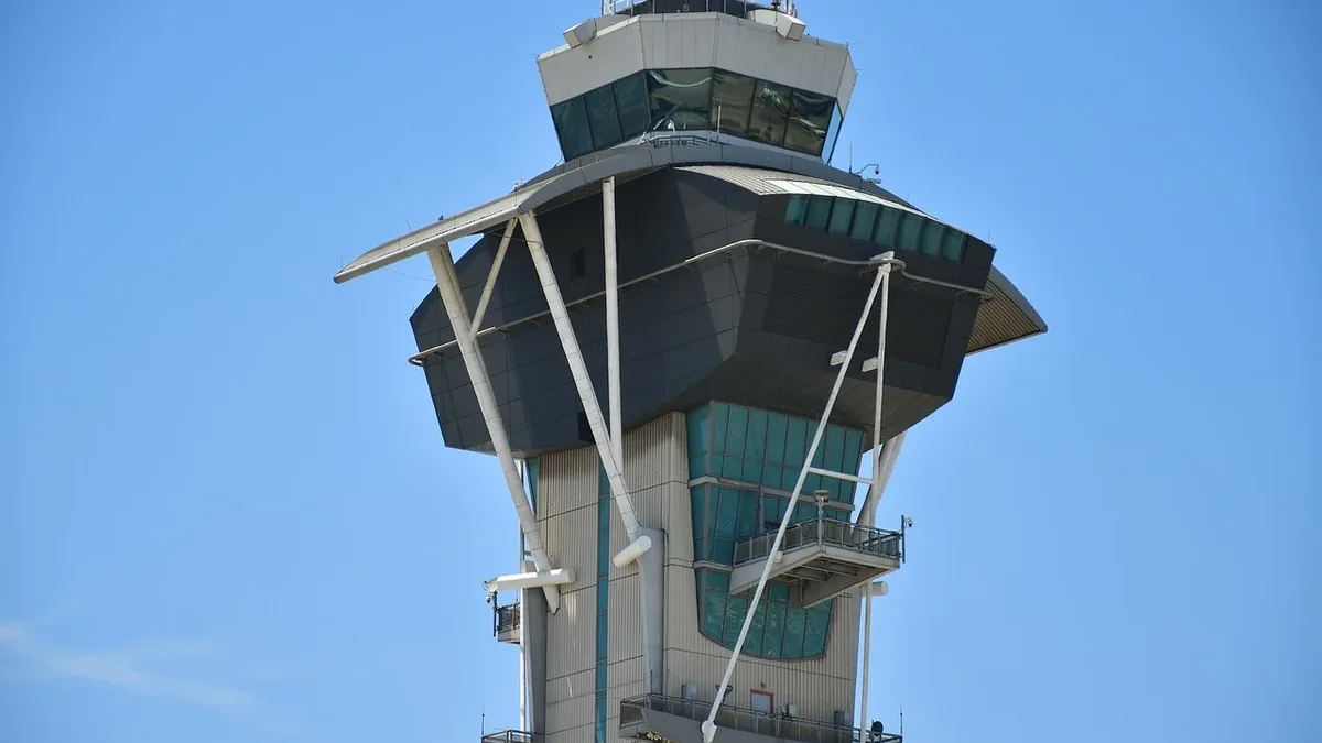 A tall air traffic control tower with a flat roof and a glass-enclosed upper level, set against a clear blue sky.