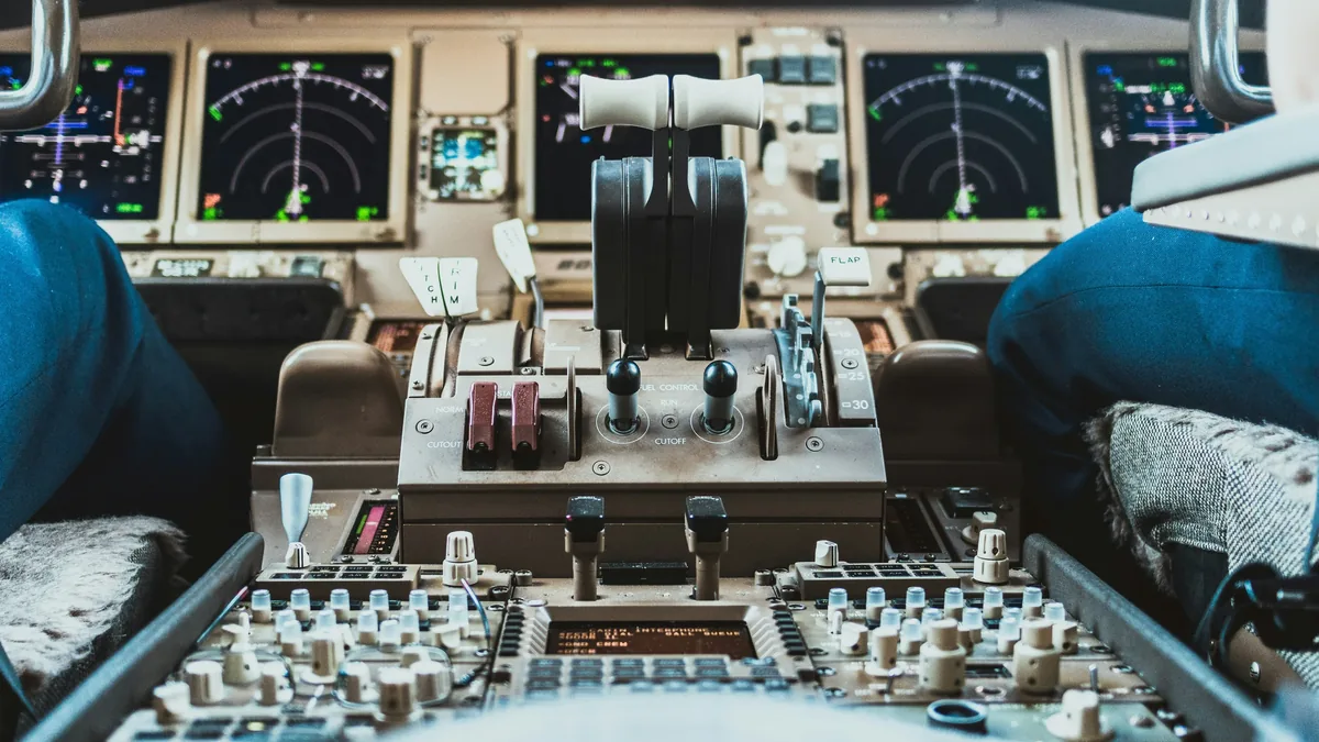 The cockpit of an airplane, featuring a control panel with various buttons and levers, as well as multiple screens displaying flight data.