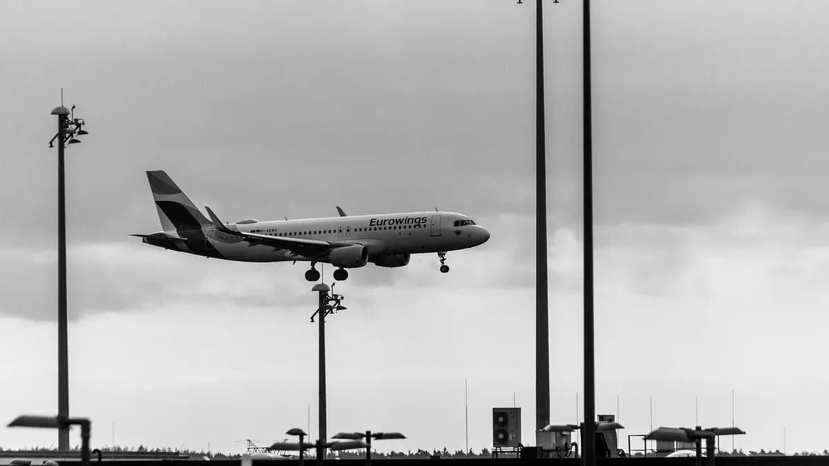 A commercial airplane is flying low over an airport, with its landing gear down.