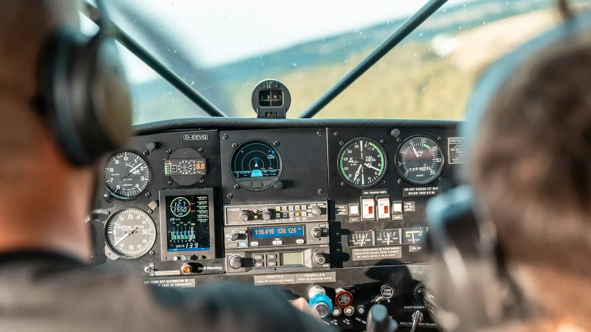 The cockpit of an airplane, with the pilot and co-pilot seated in front of a control panel featuring various instruments and controls.