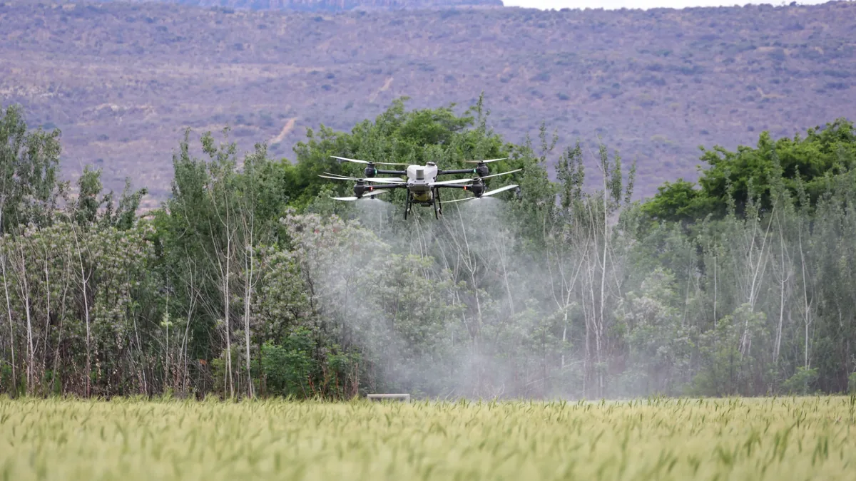 A drone flying over a field, spraying a substance onto the trees and grass.
