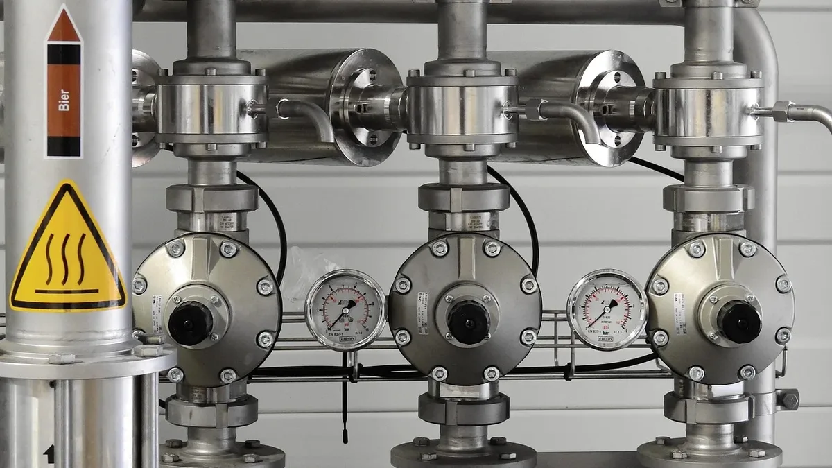 A stainless steel pipe system with valves, gauges, and warning signs.